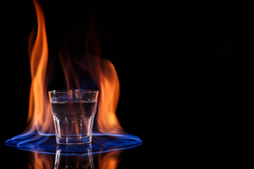 Vodka in glass and flame on black background, space for text