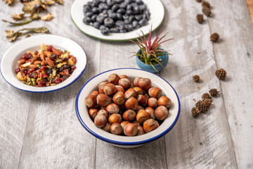 white porcelain enameled metal bowl filled with hazelnuts accompanied by others with dried fruits and blueberries