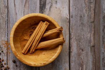 Bamboo wooden bowl with cinnamon sticks and ground cinnamon on vintage wooden table