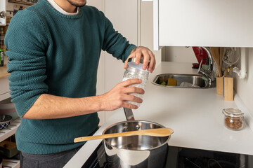 Young man's hands unscrewing a jar of sea salt to season the food he is going to prepare on a glass...