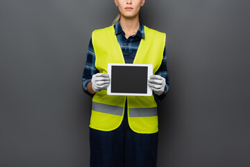 Cropped view of builder in safety vest and gloves holding digital tablet with blank screen isolated on grey