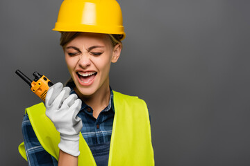 Angry builder in hardhat screaming while holding walkie talkie isolated on grey