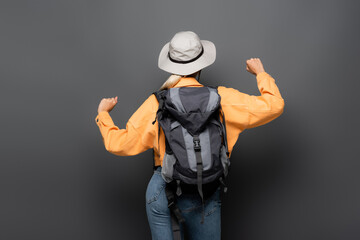 Back view of tourist with backpack showing yes gesture on grey background