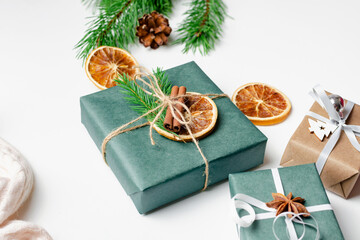 Fototapeta na wymiar Decorated christmas gift boxes with dry oranges, spices and pine tree branches on white