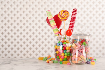 Jars with different delicious candies on white marble table, space for text