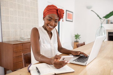 African american woman working on laptop while using phone at home
