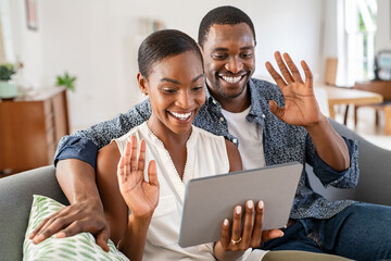 Happy smiling african couple doing video call with digital tablet at home