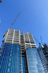 Steel and concrete construction sites of skyscrapers use hoisting towers and cranes with blue sky.