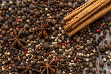 Close-up top view image with multi-colored pepper seeds, cinnamon sticks and star anise seeds on wooden table