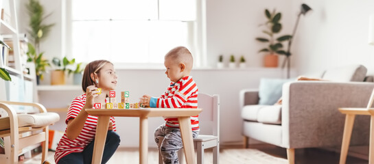 Sister teaching little brother letters by using cubes with symbols indoors.