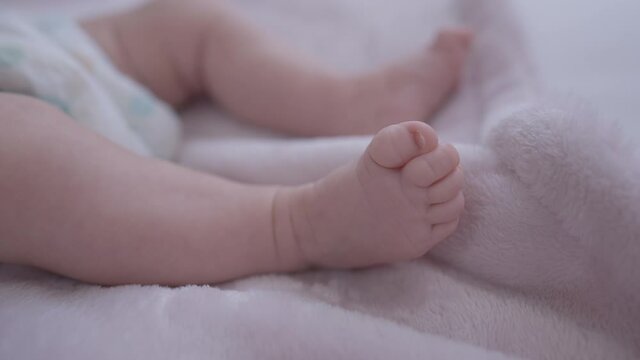 Close-up little Caucasian baby legs moving lying on soft comfortable bed indoors. Unrecognizable infant in diaper at home in bedroom. Beauty and infancy