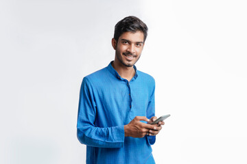 Young indian man in tradition wear and using smartphone on white background.