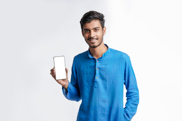 Young indian man in tradition wear and showing smartphone screen on white background.