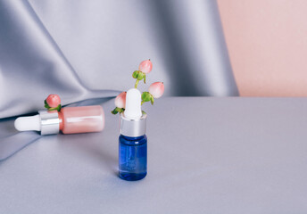 Glass bottles with hypericum on a shiny pink and gray fabric background. Serum or essential aroma oil. Focus on the blue bottle. Health and medicine concept. Front view, copy space