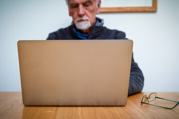Senior Man using laptop at home with close up detail on hands on keyboard