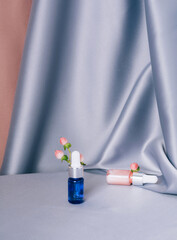 Glass bottles with hypericum on a shiny pink and gray fabric background. Serum or essential aroma oil. Focus on the pink bottle. Health and medicine concept. Front view, copy space, vertical