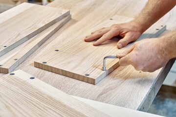 Carpenter assembles wooden furniture, twists the fittings into the veneered panel on workbench in...