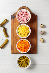 Preparations for meat salad in small white bowls. Finely chopped boiled vegetables, peas, meat or ham. Top view