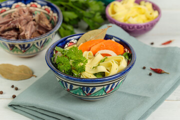Homemade noodles with vegetables and herbs, boiled meat is served separately. Close-up in painted plates. Selective focus
