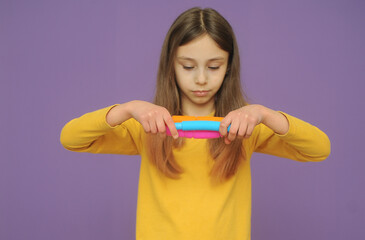 little smart girl in yellow clothes plays with trendy toy pop tube