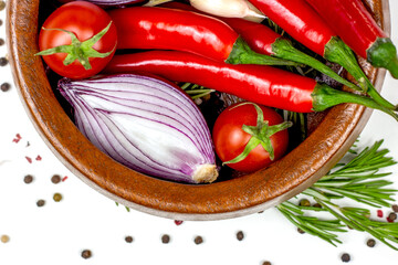 Top view of summer vegetables: onion, garlic, tomato, red chili pepper, rosemary in brown wooden bowl and peppercorns on white table background.