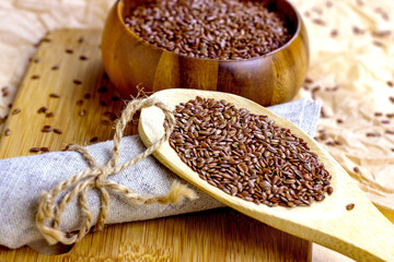 Brown raw dry flax seeds in a wooden spoon and bowl on a light background.