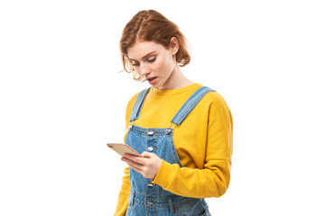 Pensive thinking redhead girl looking at smartphone screen with upset face in yellow clothes isolated on white studio background