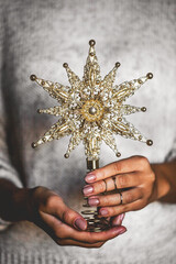 Woman in warm woolen sweater holding toy glass decorative star in hands, copy space, square crop. Christmas, new year holiday celebration concept