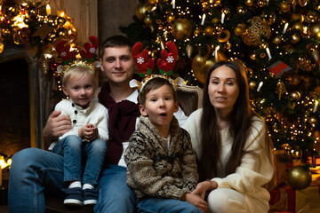 Portrait of a young family. Young parents together with their two sons are sitting on a chair against the background of a Christmas tree