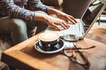 Closeup hands of Freelancer woman working using digital laptop computer and drink coffee breakfast on workplace table at cafe shop in the morning. Remote working from home. 