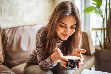 portrait of young woman drinking coffee at table in cafe. Side view of Happy brunette woman drinking coffee and looking at the camera. 