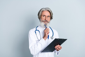 Photo of doubtful senior man doc dressed white uniform spectacles writing prescriptions looking empty space isolated grey color background