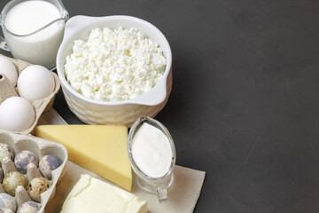 Protein food, farm dairy products on a gray background with copy space. Quail and chicken eggs, milk, cheese, butter, cream, sour cream. Source of calcium, amino acids, vitamin D, vitamin A, B6, B12