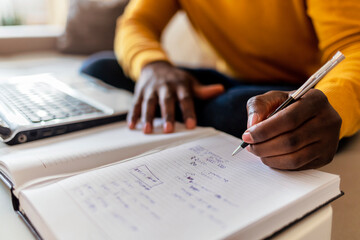 Cropped shot of an unrecognized young businessman sitting alone in his home office and writing notes. Handsome young man making notes while working at home.