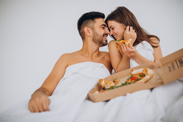 Couple eating pizza together in bed