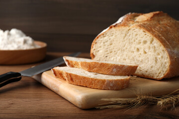 Cut tasty sodawater bread and wheat spikes on wooden table