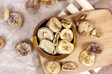 Top view of sweet dried italian figs in the wooden bowl on the brown cutting board background.