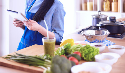 Young woman using a tablet computer to cook in her kitchen
