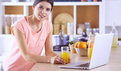 Young woman in kitchen with laptop computer looking recipes, smiling. Food blogger concept