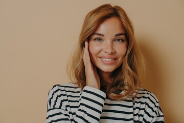 Fototapeta premium Portrait of good looking young woman touches face gently smiles toothily looks directly at camera