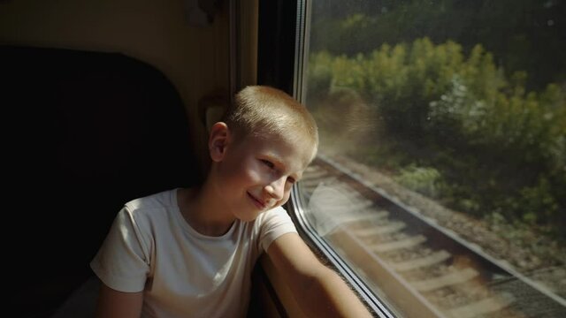 Pensive kid leaned his head against the compartment window. Boy is traveling by train. Kid looks out the train window. The child dreams of a fun summer vacation. Long-distance family trip. End of lock