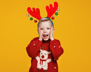 Excited boy in Christmas sweater and reindeer horns looking at camera with surprised face expression
