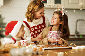 Happy family mother and two kids in festive outfit making Christmas cookies together in kitchen