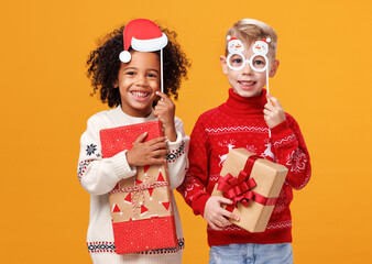 Happy multiracial children in warm knitted sweaters holding Christmas party glasses and gift boxes