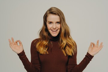 Calm young woman in casual clothes holding hands in mudra gesture, isolated on grey background