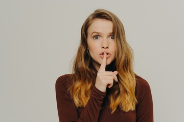Mysterious caucasian teen girl holding finger on lips, looking at camera with scared face expression