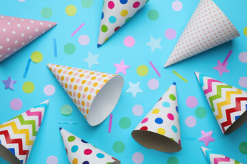 Bright party hats and confetti on light blue background, flat lay