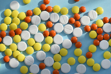 Antiviral white, yellow and orange pills for treatment on a blue background. Flat lay, top view