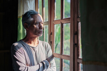 A gloomy elderly man looks out of the window thinking about personal problems. Lost in the idea of ​​a middle-aged grandfather suffering from loneliness.