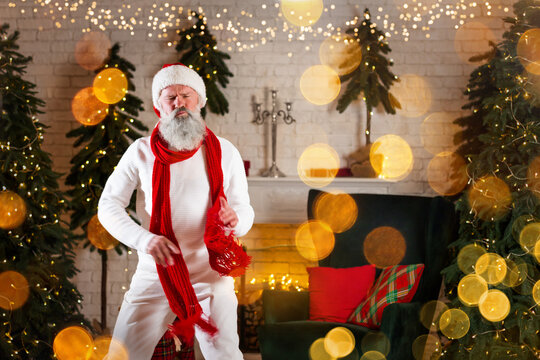 Santa Claus dancing near the fireplace and Christmas tree with gifts box, presents. New Year's cheerful mood Spirit of Merry Christmas. Senior man with real white beard cosplay Happy holidays concept